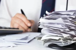 دست شخصی در حال امضای اسناد ، در کنار دسته ای کاغذ روی میز کار